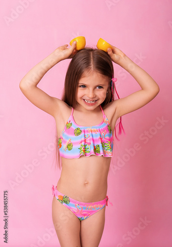 Caucasian beautiful little girl with fresh yellow lemons on a pink background. Little girl with lemon. Funny child isolated on pink.