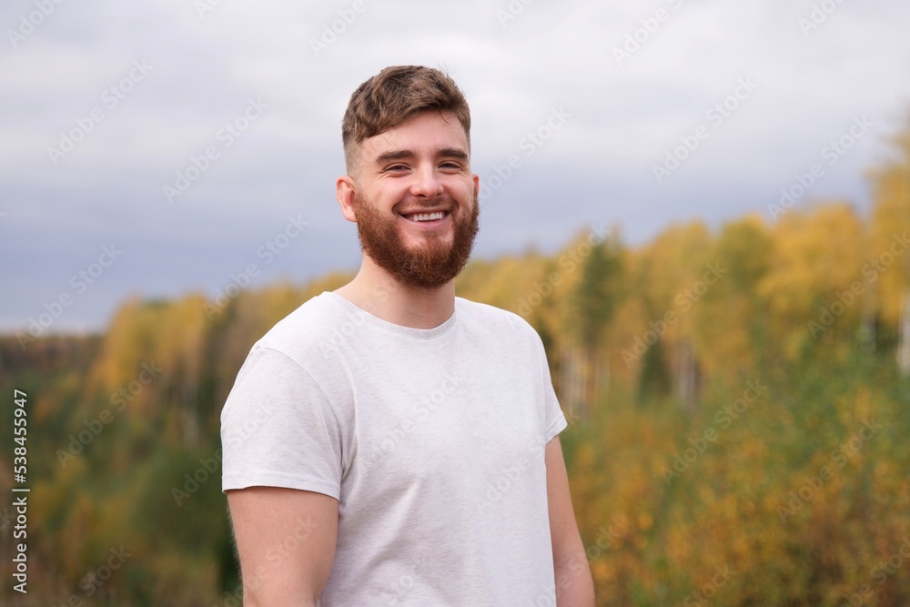 portrait of handsome bearded guy, young happy positive man with beard is smiling, laughing, walking at golden autumn or summer park, forest on natural background, looking at camera