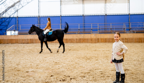 Young cute girl on a horse ranch. Cheerful pretty child on countryside.