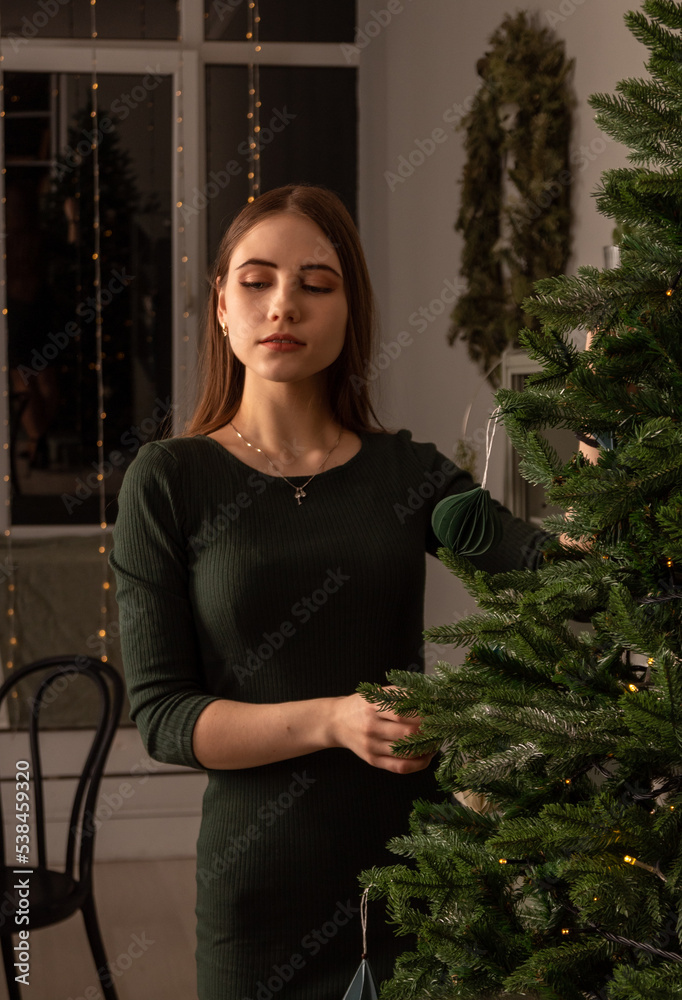Young woman in dress poses near Christmas tree. Selective focus. Images for articles about Christmas, holidays.