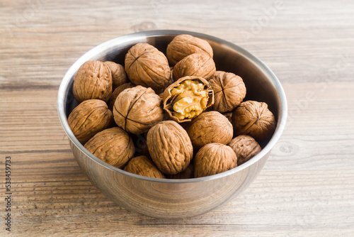 Newly harvested walnuts, designed in stainless steel bowl on a wooden table,above view