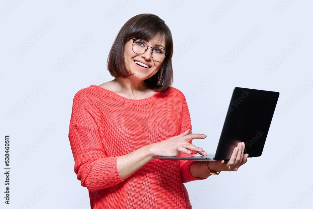 Woman with laptop in hands, looking at camera on light studio background Woman with laptop in hands, looking at camera on light studio background
