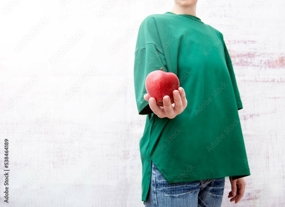 A woman in a green T-shirt holds a ripe red apple in her hand. Selective focus.