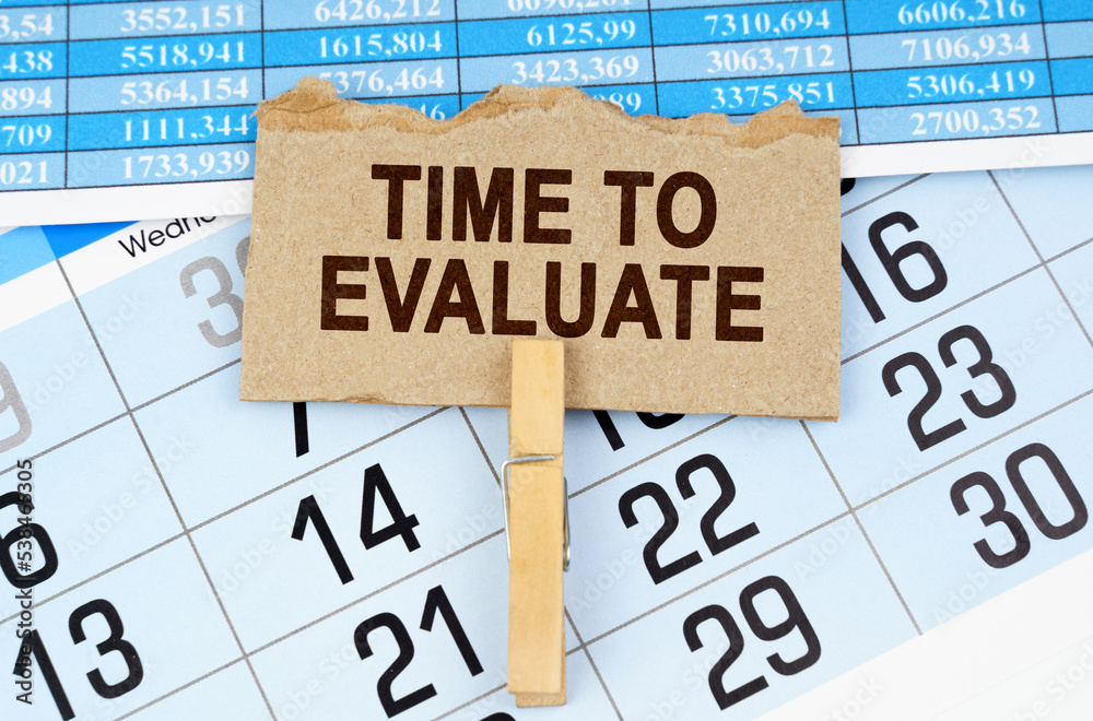 On the calendar and reporting documents is a cardboard plate with the inscription - TIME TO EVALUATE On the calendar and reporting documents is a cardboard plate with the inscription - TIME TO EVALUATE