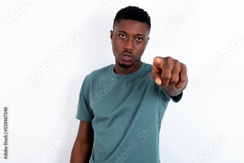 Cheerful young handsome man wearing green T-shirt over white background indicates happily at you, chooses to compete, has positive expression, makes choice.