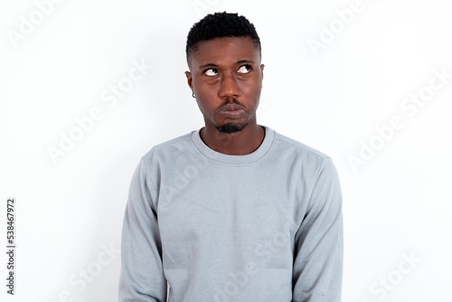 Dissatisfied young handsome man wearing grey sweater over white background purses lips and has unhappy expression looks away stands offended. Depressed frustrated model.