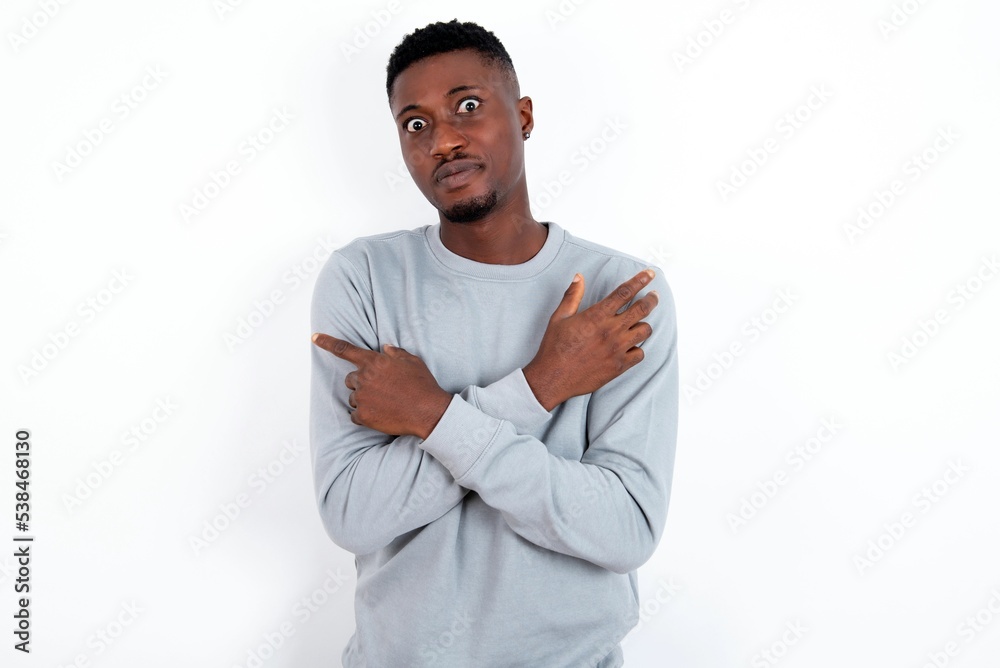 Serious young handsome man wearing grey sweater over white background crosses hands and points at different sides hesitates between two items. Hard decision concept Serious young handsome man wearing grey sweater over white background crosses hands and points at different sides hesitates between two items. Hard decision concept