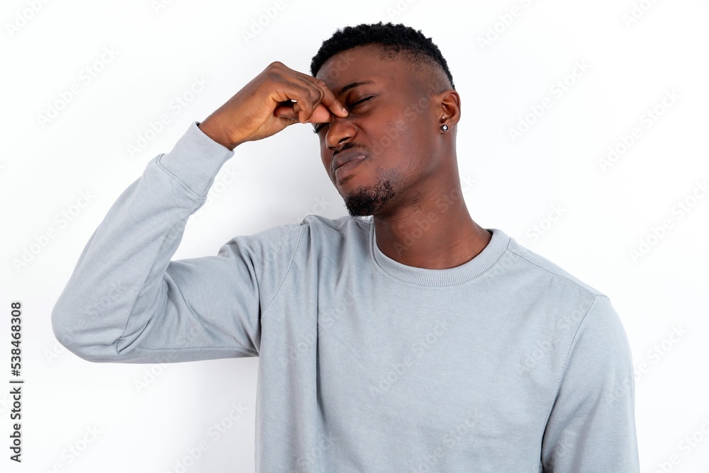 Sad young handsome man wearing grey sweater over white background suffering from headache holding hand on her face Sad young handsome man wearing grey sweater over white background suffering from headache holding hand on her face