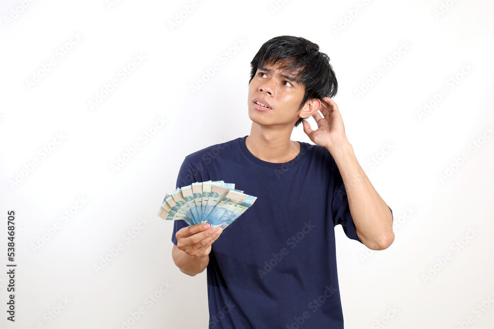 Thoughtful and daydreamed young asian man standing while holding Indonesian banknotes. Isolated on white Thoughtful and daydreamed young asian man standing while holding Indonesian banknotes. Isolated on white