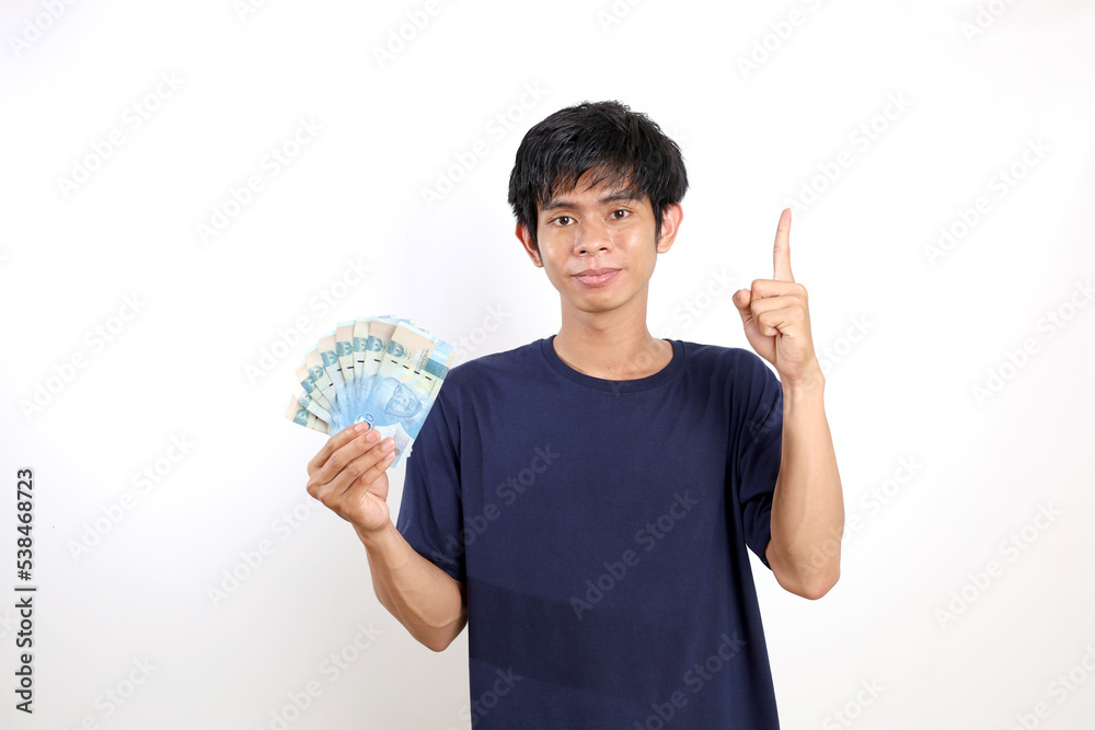 Happy Young asian man standing while holding Indonesian banknotes and showing one finger or pointing above Happy Young asian man standing while holding Indonesian banknotes and showing one finger or pointing above