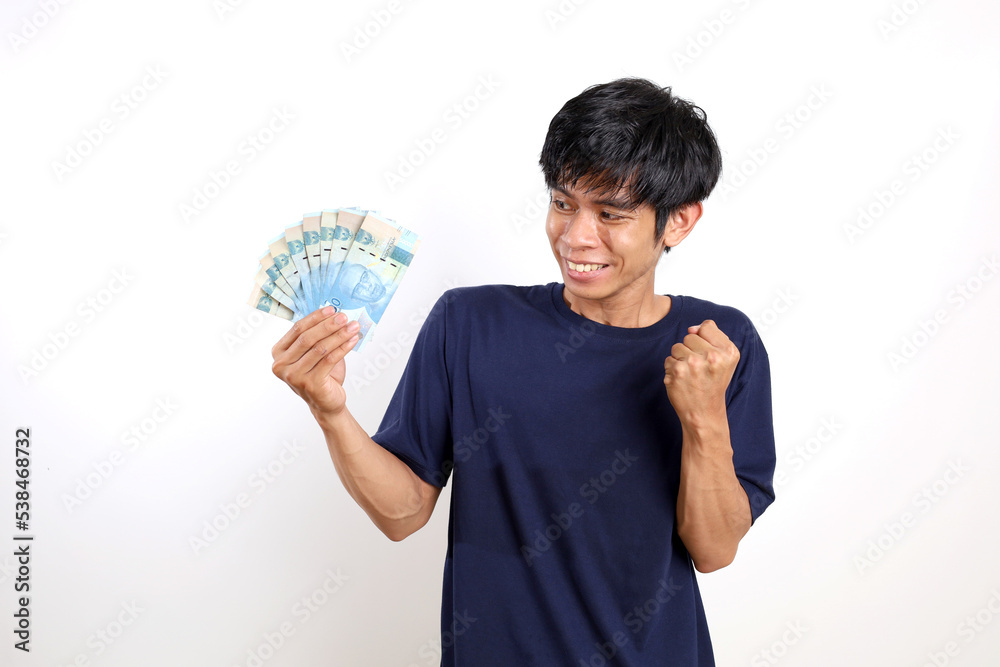 Happy young asian man in t-shirt standing while holding Indonesian banknotes. Isolated on white background