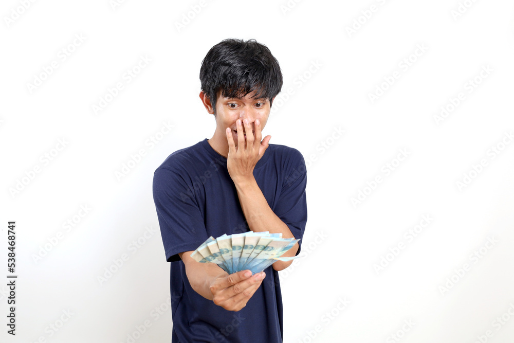 Amazed and surprised young asian man standing while holding Indonesian banknotes. Isolated on white Amazed and surprised young asian man standing while holding Indonesian banknotes. Isolated on white