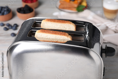Modern toaster with bread on white wooden table, closeup