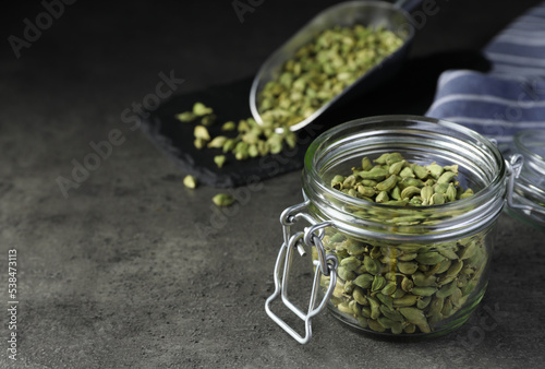 Glass jar with dry cardamom pods on dark grey table, space for text