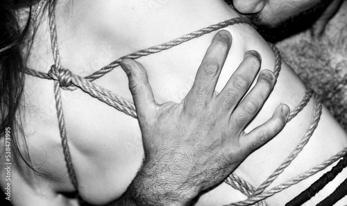 A young, slim, naked hot woman with knots of natural ropes kissed by her boyfriend. Ancient Japanese art of aesthetic bondage and tying shibari kinbaku. Concept of BDSM sex games. Black and white. BNW photo