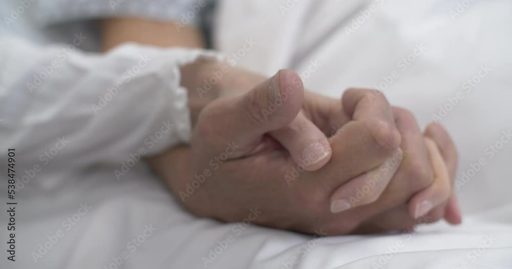 Man and woman hold hands in hospital bed interlocking fingers healthcare patient