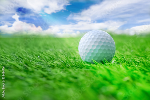 golf ball on green grass with blue sky background.