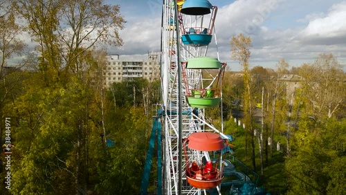 Aerial around view of the city ferris wheel in a golden autumn amusement park under light blue cloudy sky, drone flying inside