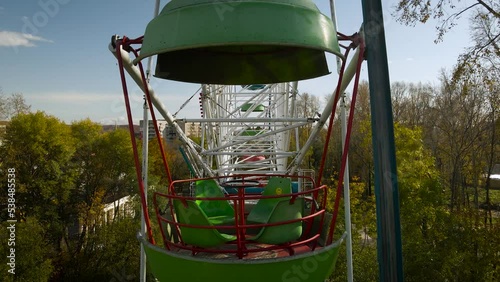 Aerial around view of the city ferris wheel in the golden autumn amusement park under light blue cloudy sky, drone flying inside