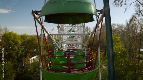Aerial around view of the city ferris wheel in the golden autumn amusement park under light blue cloudy sky, flying inside
