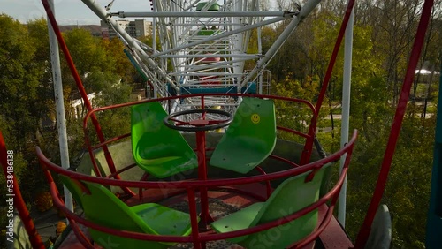 Aerial around view of the city ferris wheel with bucket seat in golden autumn amusement park under light blue cloudy sky, drone flying inside