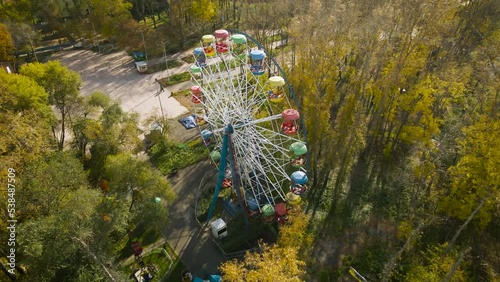 Aerial view of the city ferris wheel with bucket seat in golden autumn amusement park under light blue cloudy sky