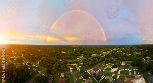 Colorful round rainbow over rural town suburbs against blue evening sky after heavy thunderstorm