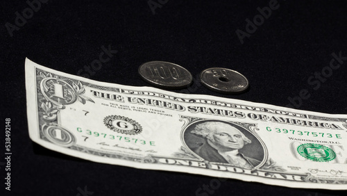 150 Japanese Yens in 100 and 50 yen coins placed on top of a falling US $1 bill. Solid plain black background. Blank copy space for text or additional design. photo