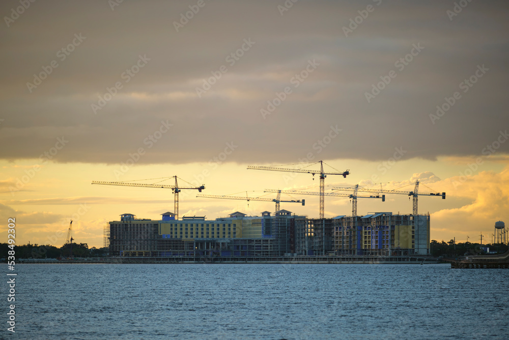 Tower cranes and frame structure of high residential apartment buildings at construction site on sea bay shore. Real estate development at waterfront