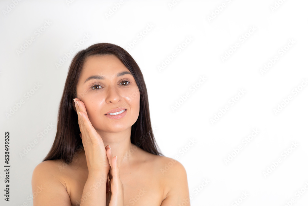 A natural portrait of a well-groomed young brunette woman with nude makeup. Gentle Beauty keeps her hands close to her face. White background place for text A natural portrait of a well-groomed young brunette woman with nude makeup. Gentle Beauty keeps her hands close to her face. White background place for text