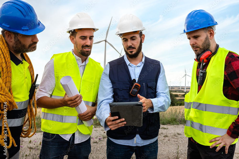 Electric engineer, explaining maintenance workers plans for wind turbine farm.Renewable energy. Electric engineer, explaining maintenance workers plans for wind turbine farm.Renewable energy.
