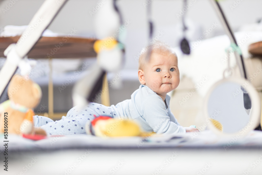 Cute baby boy playing with hanging toys arch on mat at home Baby activity and play center for early infant development. Baby playing at home Cute baby boy playing with hanging toys arch on mat at home Baby activity and play center for early infant development. Baby playing at home