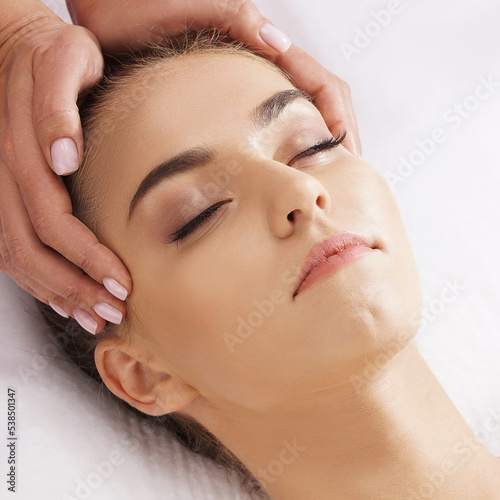 Beautiful, young and healthy woman having face massage in spa salon. Hands of professinal masseur. Spa, health and healing concept.