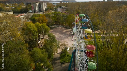 Aerial around along view of the city ferris wheel in the golden autumn amusement park under light blue cloudy sky