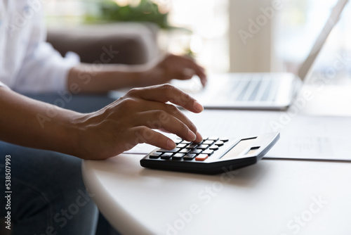 Unrecognizable female hands use calculator and laptop seated at table, close up. Unknown woman paying bills through e-bank application, accountant working, prepare financial report. Savings, finances