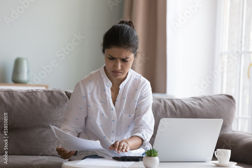 Photo Young frowning Indian woman sit on sofa sorts out household bills, utilities, ca