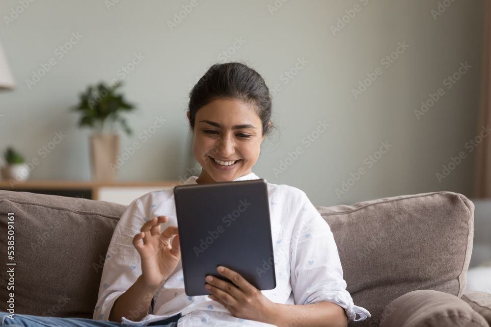 Electronic commerce client make order or buying goods and e-services on internet use website or new application for easy and comfort life. Indian woman sits on sofa with modern digital tablet device Electronic commerce client make order or buying goods and e-services on internet use website or new application for easy and comfort life. Indian woman sits on sofa with modern digital tablet device