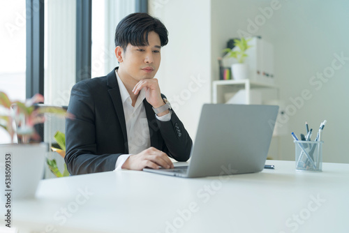 Attractive businessman working on laptop in workstation office.