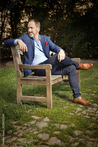 Man in blue suit with shirt and tie posing on bench in summer park © Couperfield