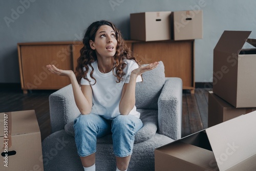 Puzzled divorced girl exclaims shrugging sitting with boxes for relocation. Divorce, hard moving day