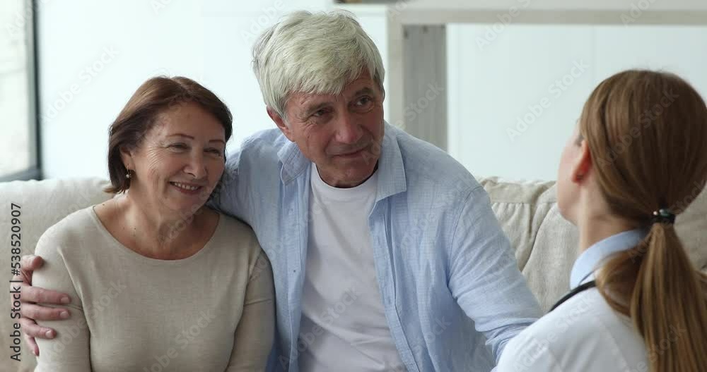 Attractive senior couple sit on couch at home receive medical consultation during female general practitioner visit, close up. Housecall, healthcare of older citizen, health check up, medicine concept Attractive senior couple sit on couch at home receive medical consultation during female general practitioner visit, close up. Housecall, healthcare of older citizen, health check up, medicine concept
