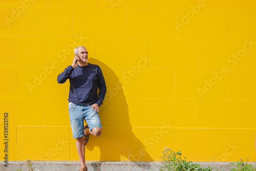 mature man talking on mobile phone on yellow wall © tetxu