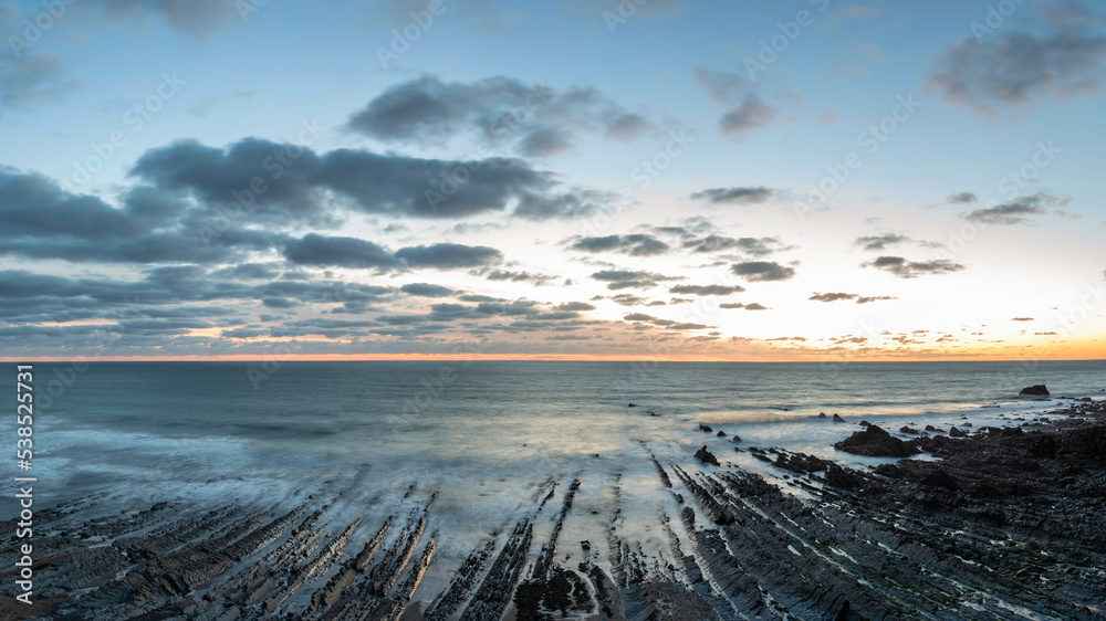 Beautiful sunset landscape image of Welcome Mouth Beach in Devon England with beautiful rock formations