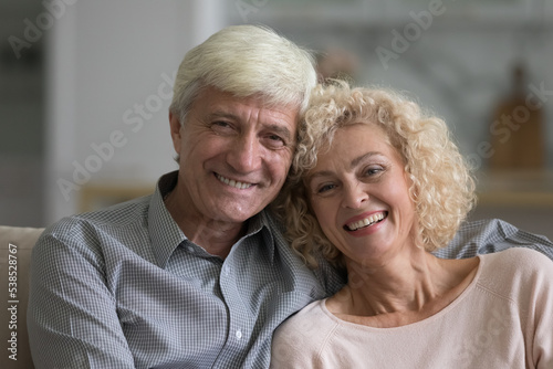 Portrait of attractive optimistic older spouses, close up shot. Happy marriage, harmonic relationships, homeowners loving couple with wide toothy smile staring at camera posing at modern home. Love