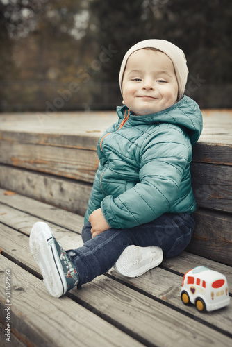 Fotografia Little boy in autumn park posing for portrait on wooden bench