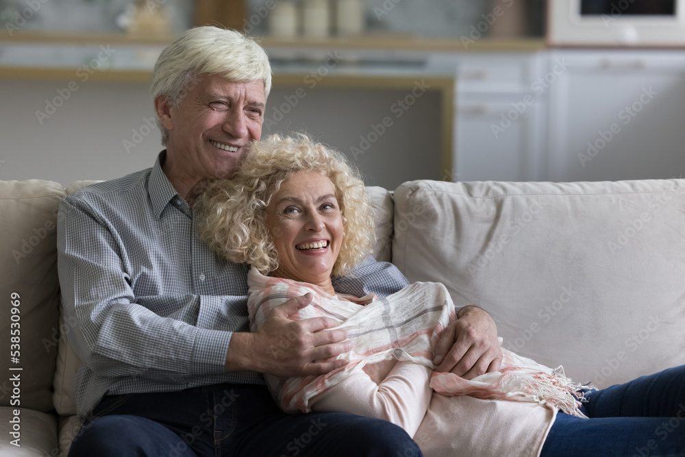 Attractive loving older spouses resting together on comfortable sofa feeling satisfied enjoy relaxation and carefree life on retirement at modern home. Romantic relationship, happy marriage, leisure Attractive loving older spouses resting together on comfortable sofa feeling satisfied enjoy relaxation and carefree life on retirement at modern home. Romantic relationship, happy marriage, leisure