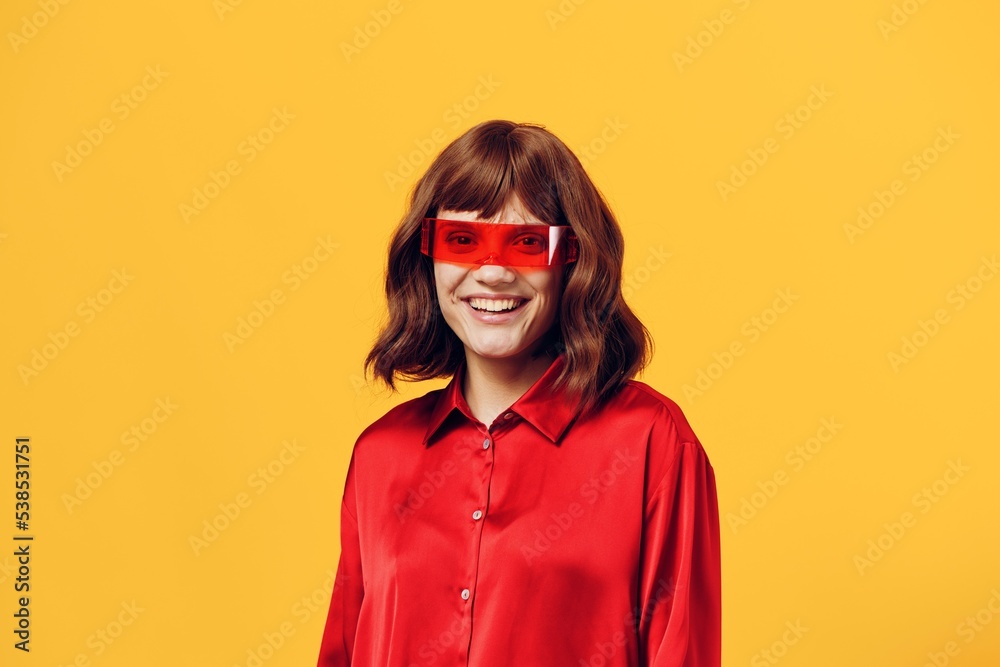 a stylish woman stands on a yellow background in a red shirt and glasses of an interesting shape smiling pleasantly at the camera a stylish woman stands on a yellow background in a red shirt and glasses of an interesting shape smiling pleasantly at the camera