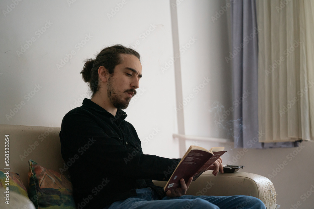 man sitting on sofa reading book and smoking cigarette man sitting on sofa reading book and smoking cigarette