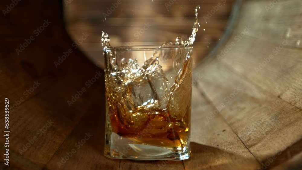 Super Slow Motion Shot of Ice Cube Falling into Glass of Whiskey inside Wooden Barrel at 1000fps.