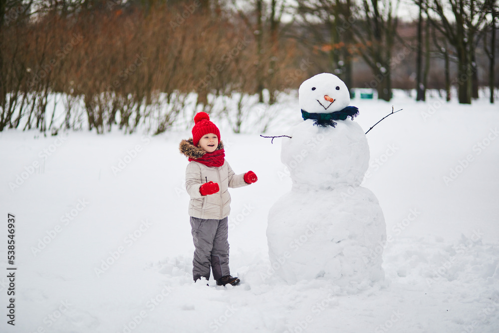 Adorable preschooler girl building a snowman on a day with heavy snowfall